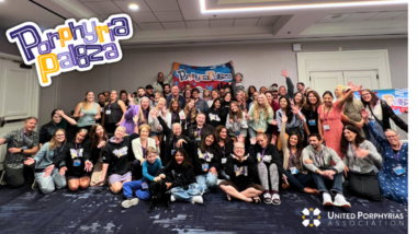 A large group of people - all from the porphyria community - pose for a group photo. Some are holding banners that read "PorphyriaPalooza."